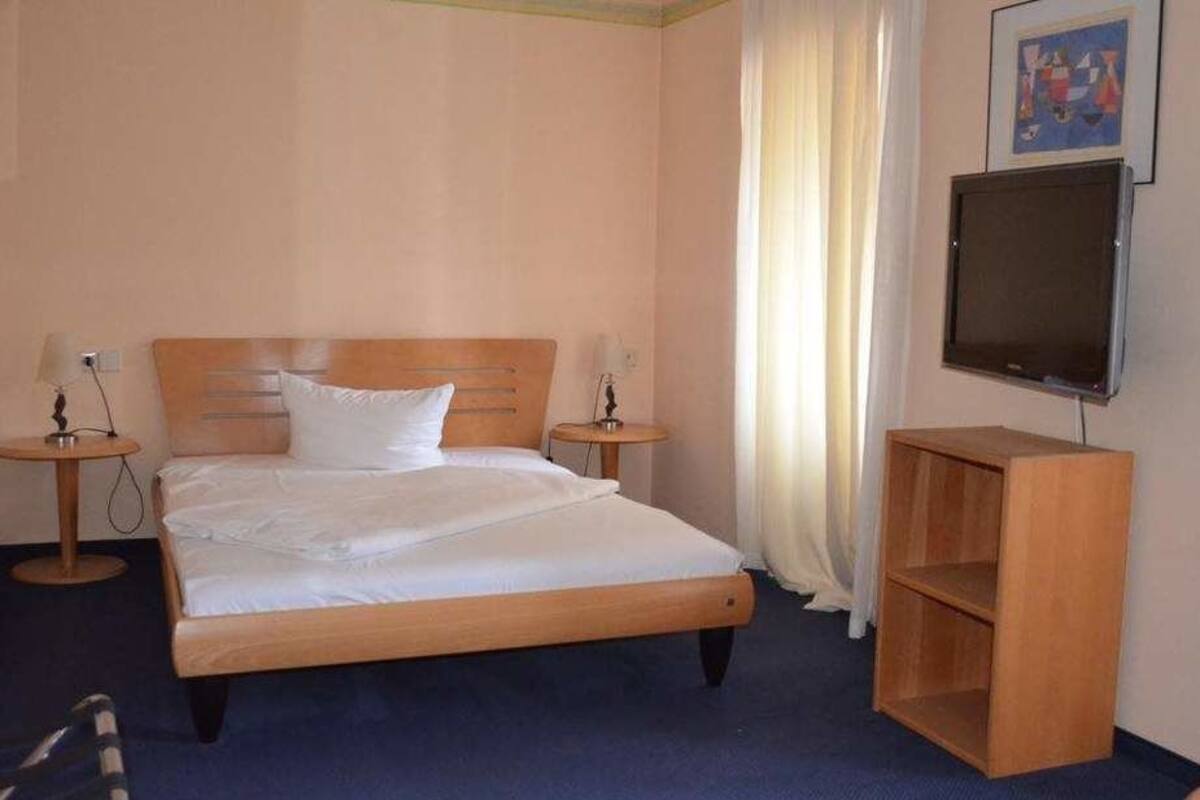 Una habitación de hotel con una cama de madera, dos mesitas de noche, un televisor y un armario de madera.