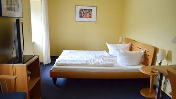 A hotel room with a bed, a desk, a chair, a television, and a picture on the wall.
