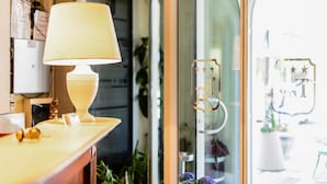 A well-lit room with a lamp on a wooden table, a glass door with a decorative handle, and a view of the outside through the glass. - Villa Adriana (Viareggio)