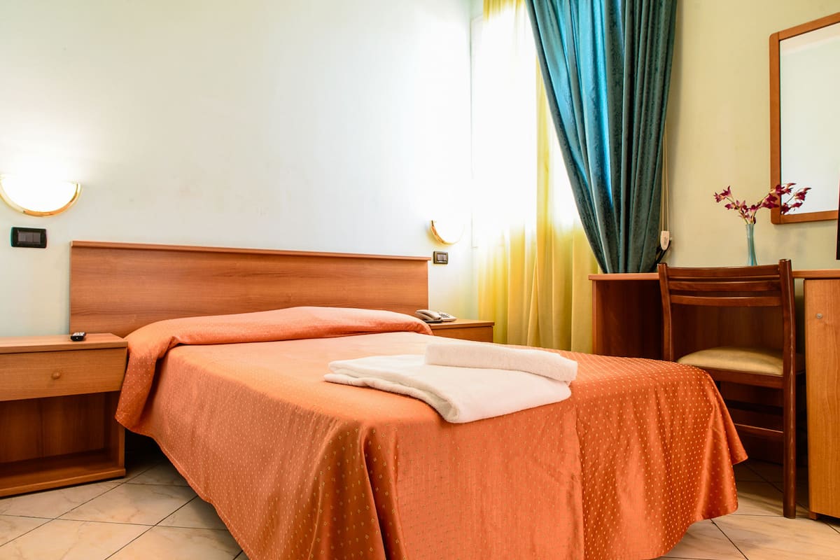 A hotel room with a wooden bed, a nightstand, a chair, a desk, and a mirror.