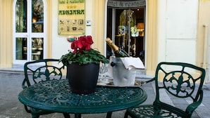 A green metal table with a potted plant and a champagne bucket outside a hotel. - Villa Adriana (Viareggio)
