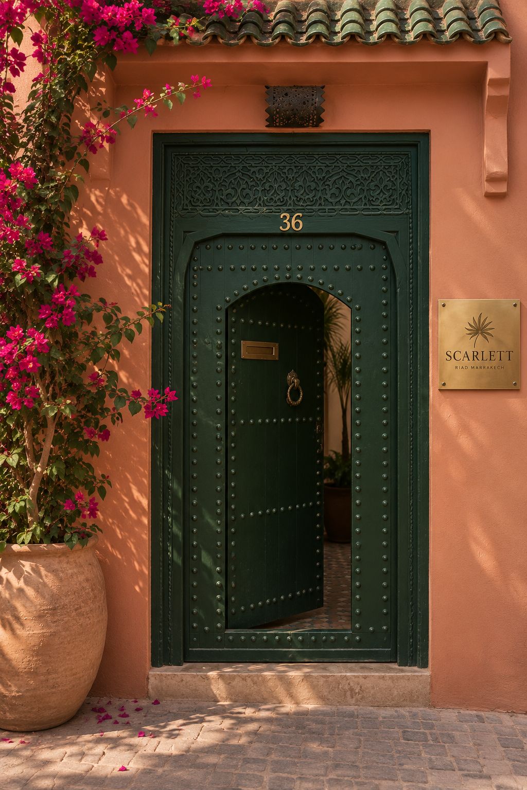 A green door with a number '36' above it, a plaque with the name 'Scarlett' on the wall, and a potted plant with pink flowers to the left.