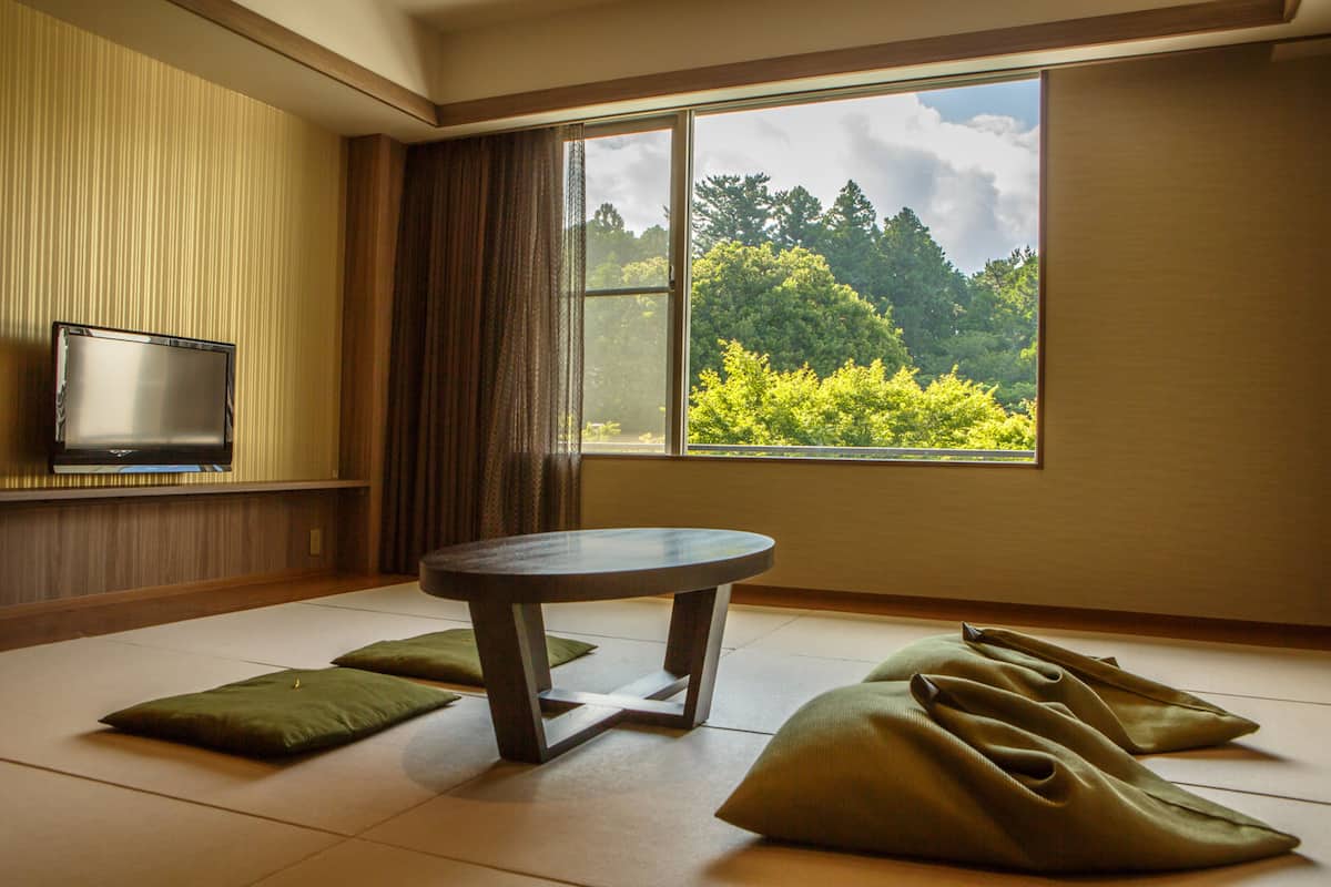 A room with tatami mats, a low table, and a TV on the wall.