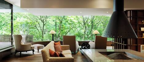 A modern living room with a fireplace, comfortable seating, and large windows offering a view of lush greenery.