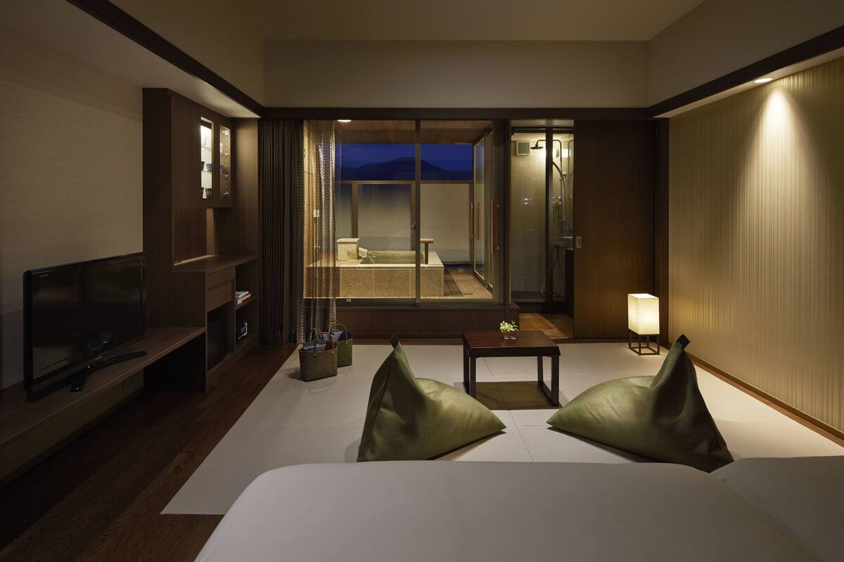 A hotel room with a bed, a television, a small table, and a view of the outdoors.