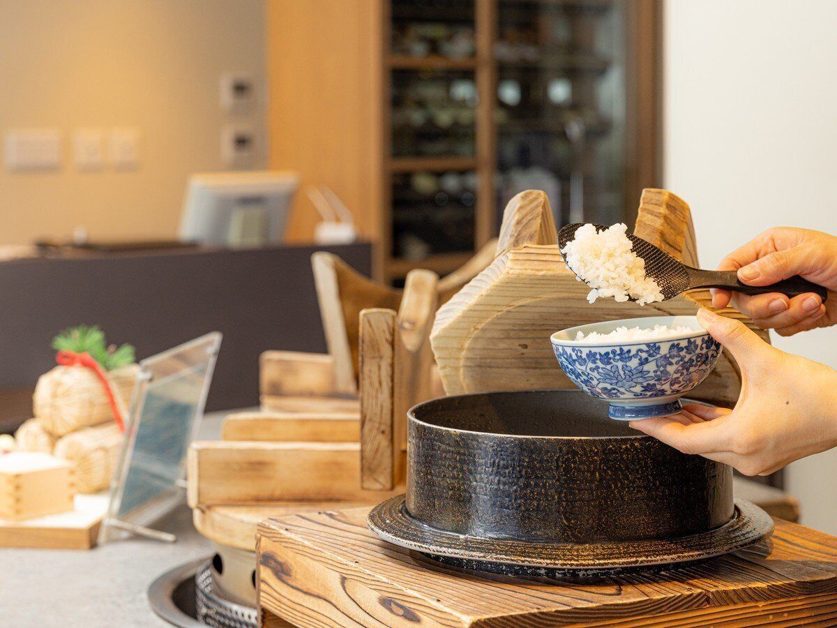 Una persona sirve arroz de un bol a una olla sobre una mesa de madera.