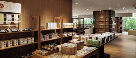 Un espacio comercial moderno con estanterías de madera que exhiben diversos productos, una mesa de madera central con artículos y una gran librería.