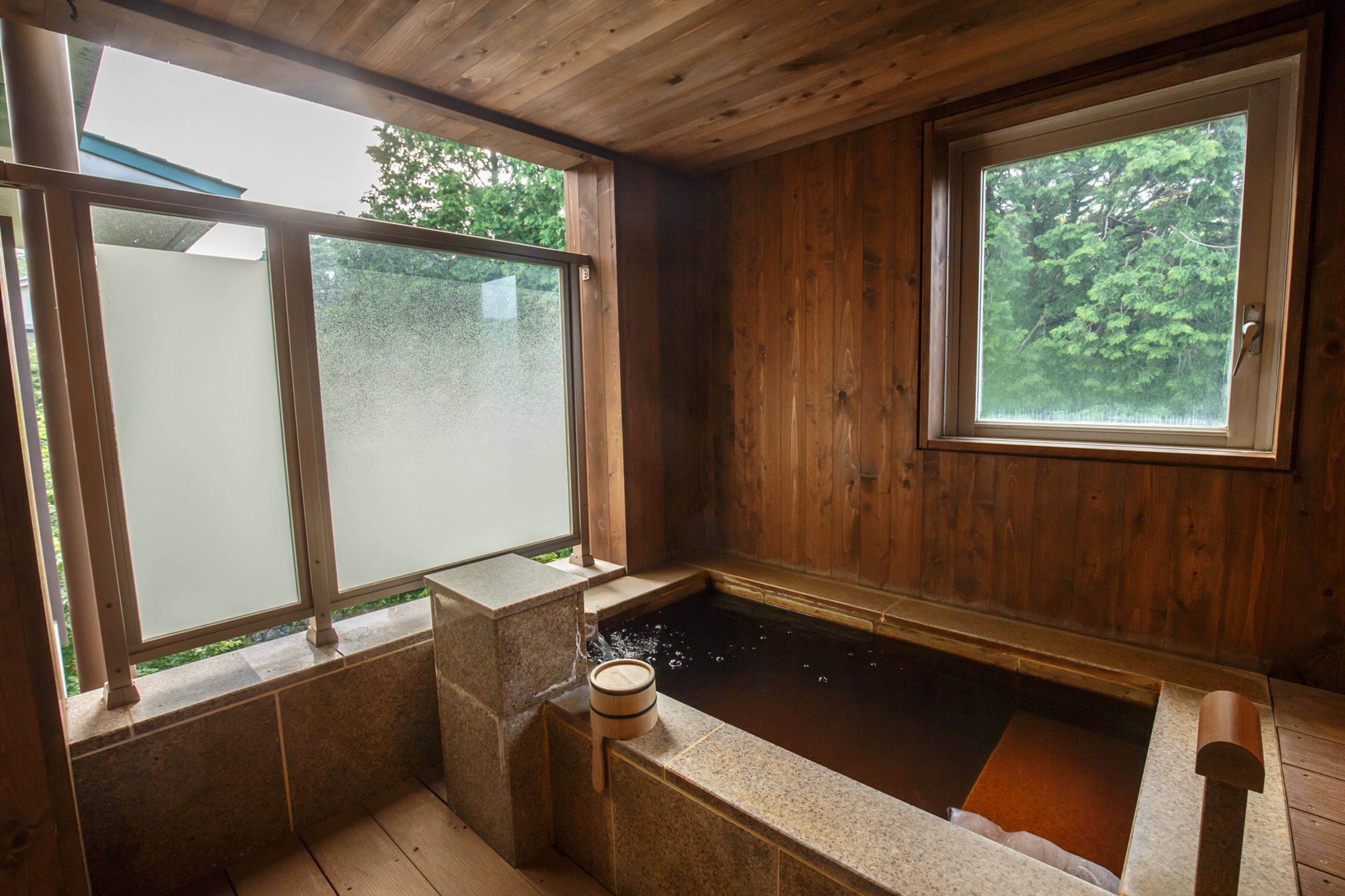 Una habitación de madera con una bañera de piedra, ventanas amplias y vistas a árboles.