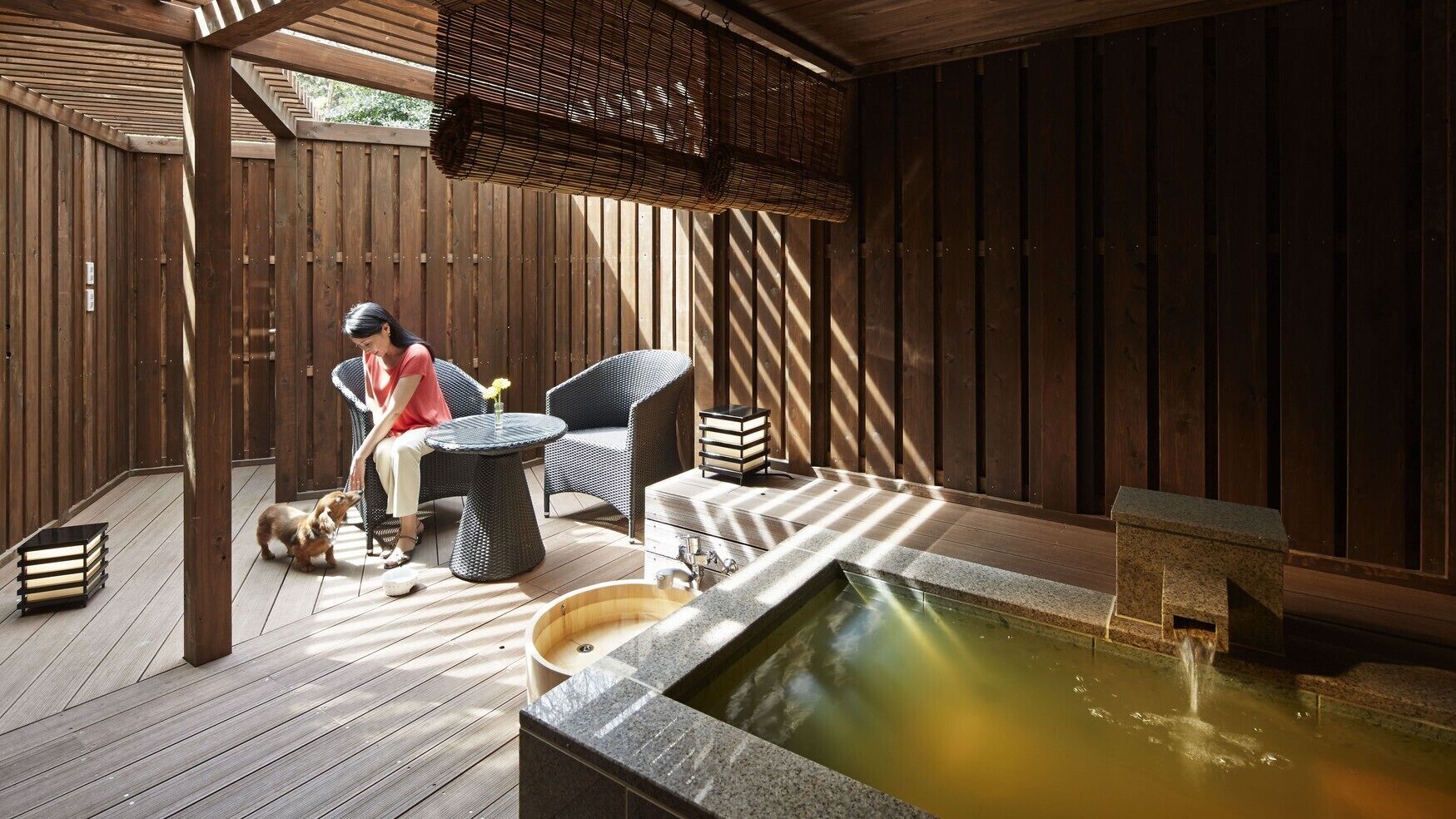Een houten terras met een jacuzzi, rieten meubels en een persoon zittend.