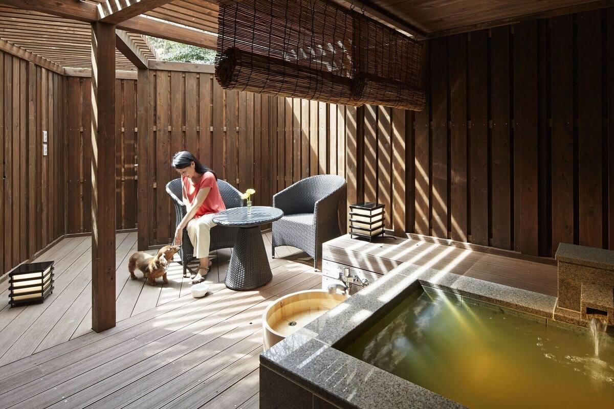 A wooden deck with a hot tub, wicker furniture, and a person sitting.