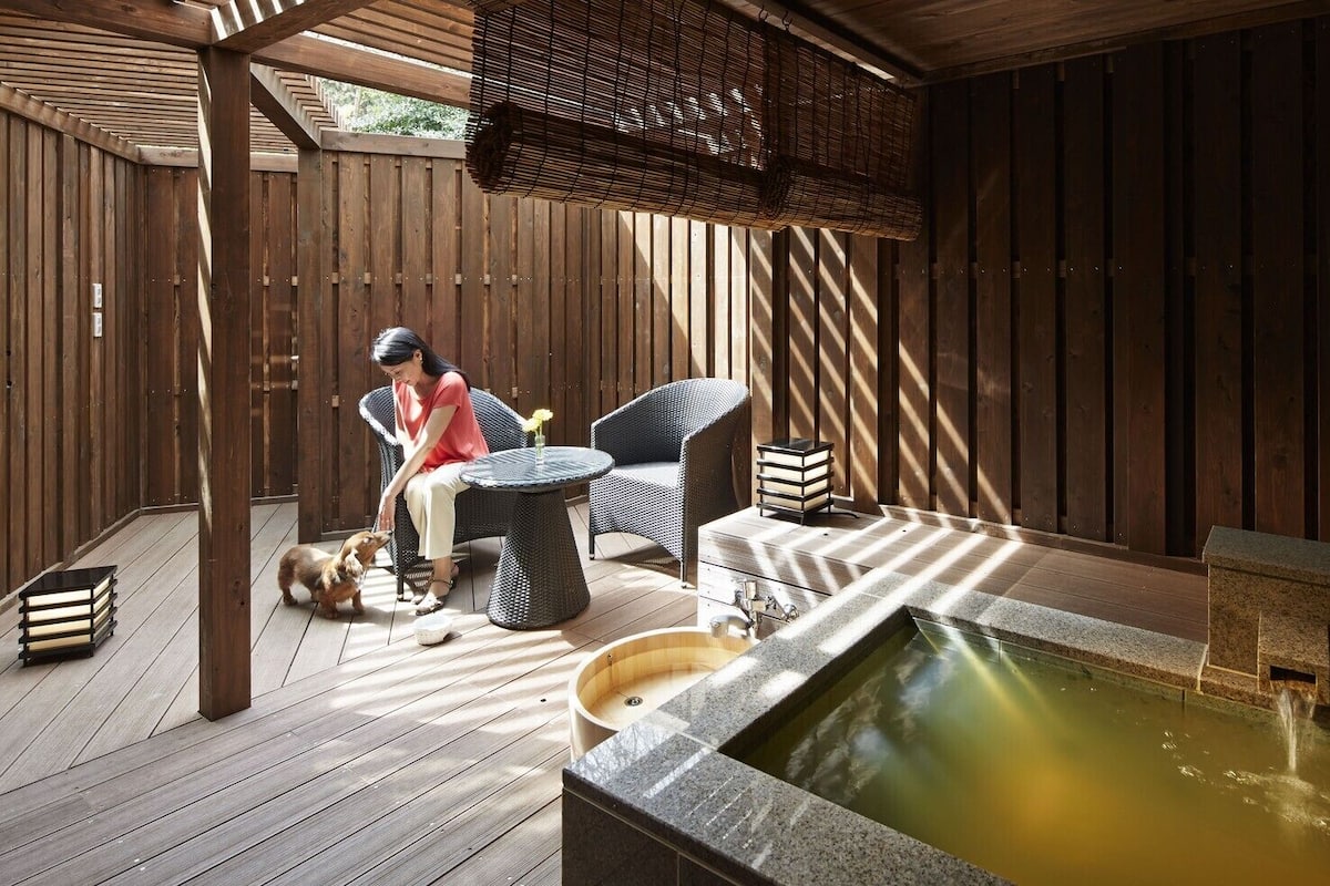 Eine Holzterrasse mit Whirlpool, Korbmöbeln und einer sitzenden Person.