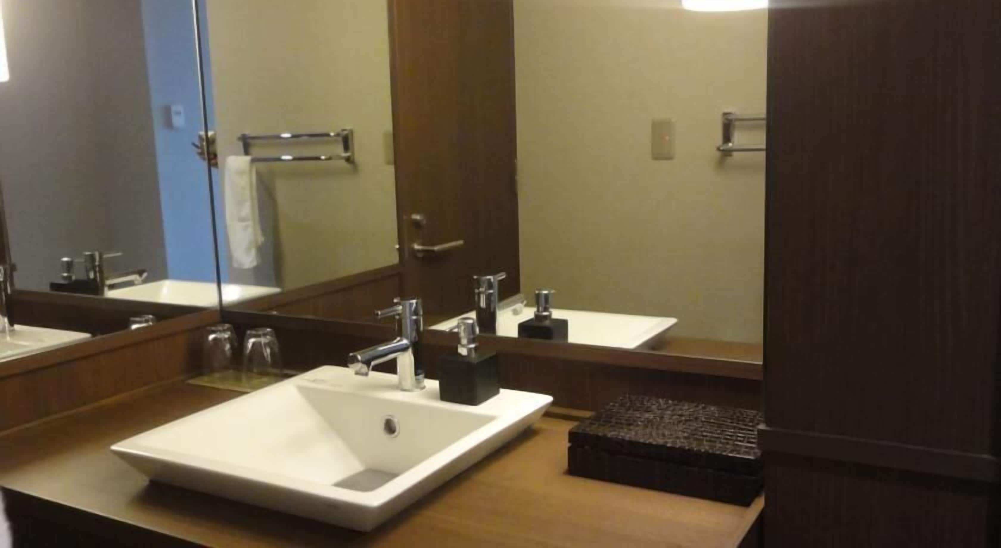 A bathroom with a white sink, two faucets, a mirror, and a towel rack.