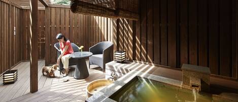 Una terraza de madera con un jacuzzi, un perro y una persona sentada en una silla.