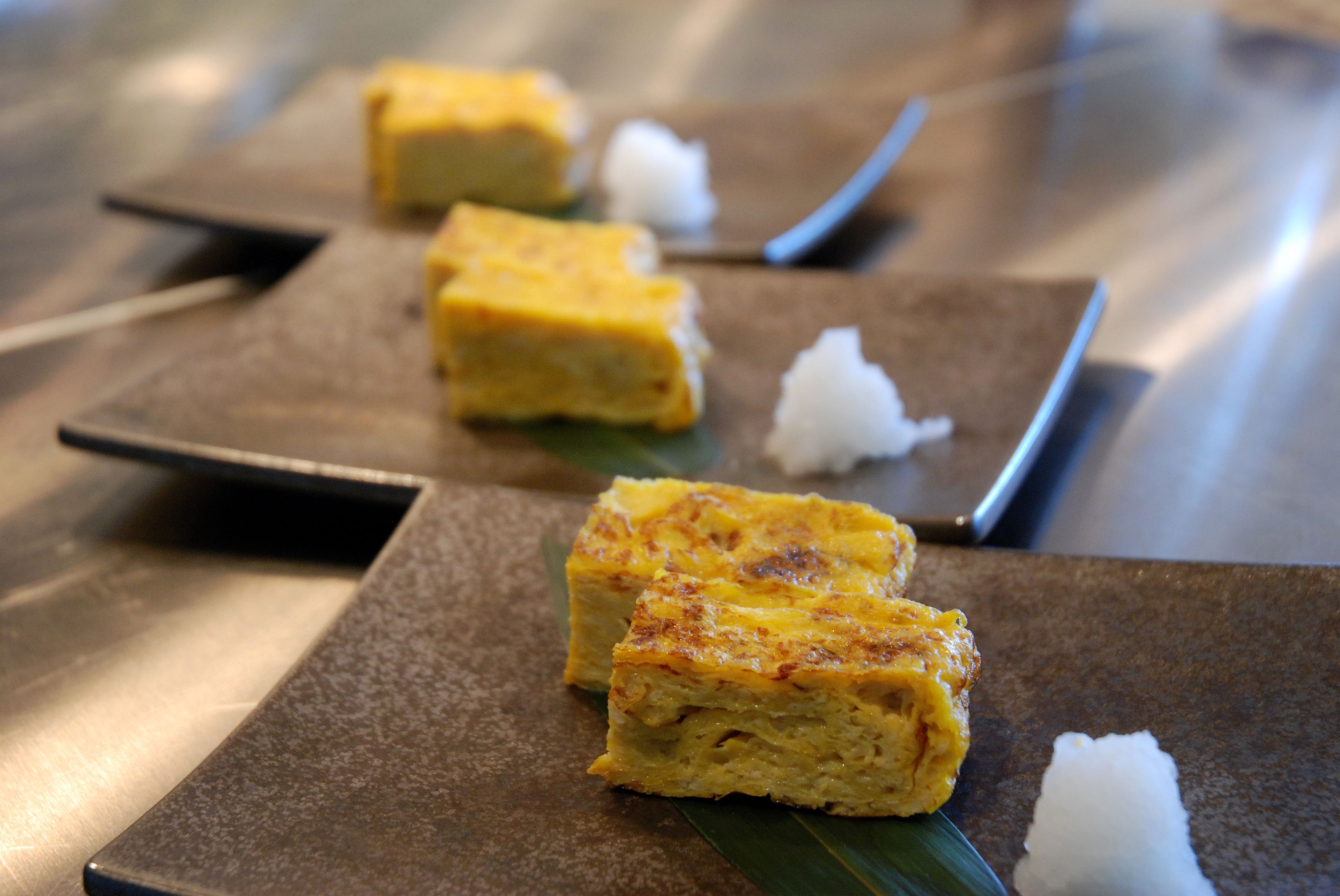A dessert with a golden-brown top, served on square plates with a dark background.