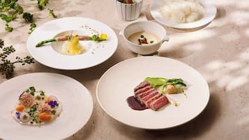 A table with various dishes including a plate of steak, a bowl of soup, and a plate of rice.