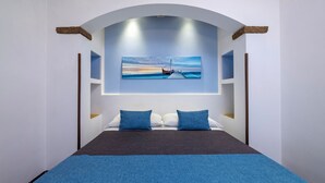 A modern hotel room with a large bed, a view of the sea through an arched window, and a painting of a boat on the water. - B&B L'Angolino della Nonna (San Vito Lo Capo)