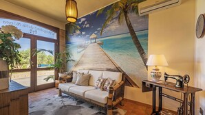 A room with a beach mural, a sofa, a table with a sewing machine, and a potted plant. - B&B L'Angolino della Nonna (San Vito Lo Capo)