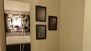 A room with a large abstract painting, three framed pictures on the wall, a red chair, and a small potted plant. - Luleå Bed & Breakfast (Luleå)
