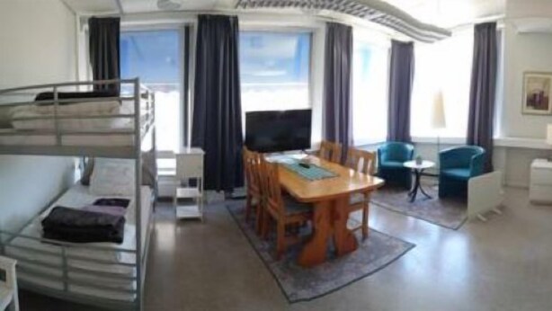 A hotel room with a bunk bed, a dining table with chairs, a TV, a small round table, a sofa, a dresser, and a window with curtains. - Luleå Bed & Breakfast (Luleå)