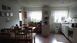 A dining area with wooden chairs and a table, a kitchen with a microwave and stove, and a clock on the wall. - Luleå Bed & Breakfast (Luleå)