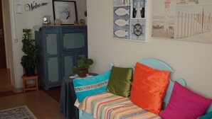A cozy living room with a light blue sofa adorned with colorful pillows, a patterned rug, and wall art depicting nautical themes. - Luleå Bed & Breakfast (Luleå)