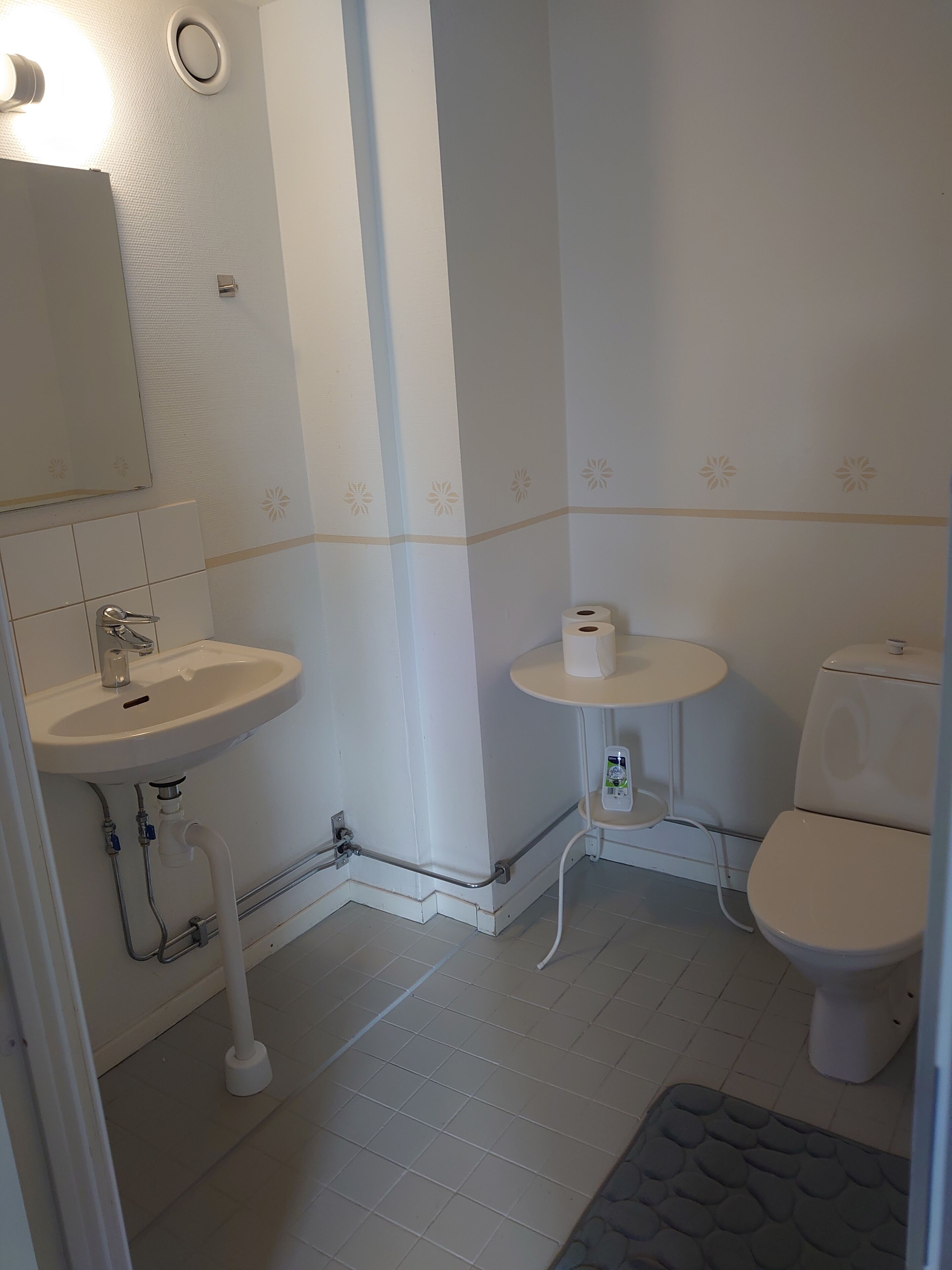 A bathroom with a sink, toilet, and a small round table with a bottle of hand sanitizer.