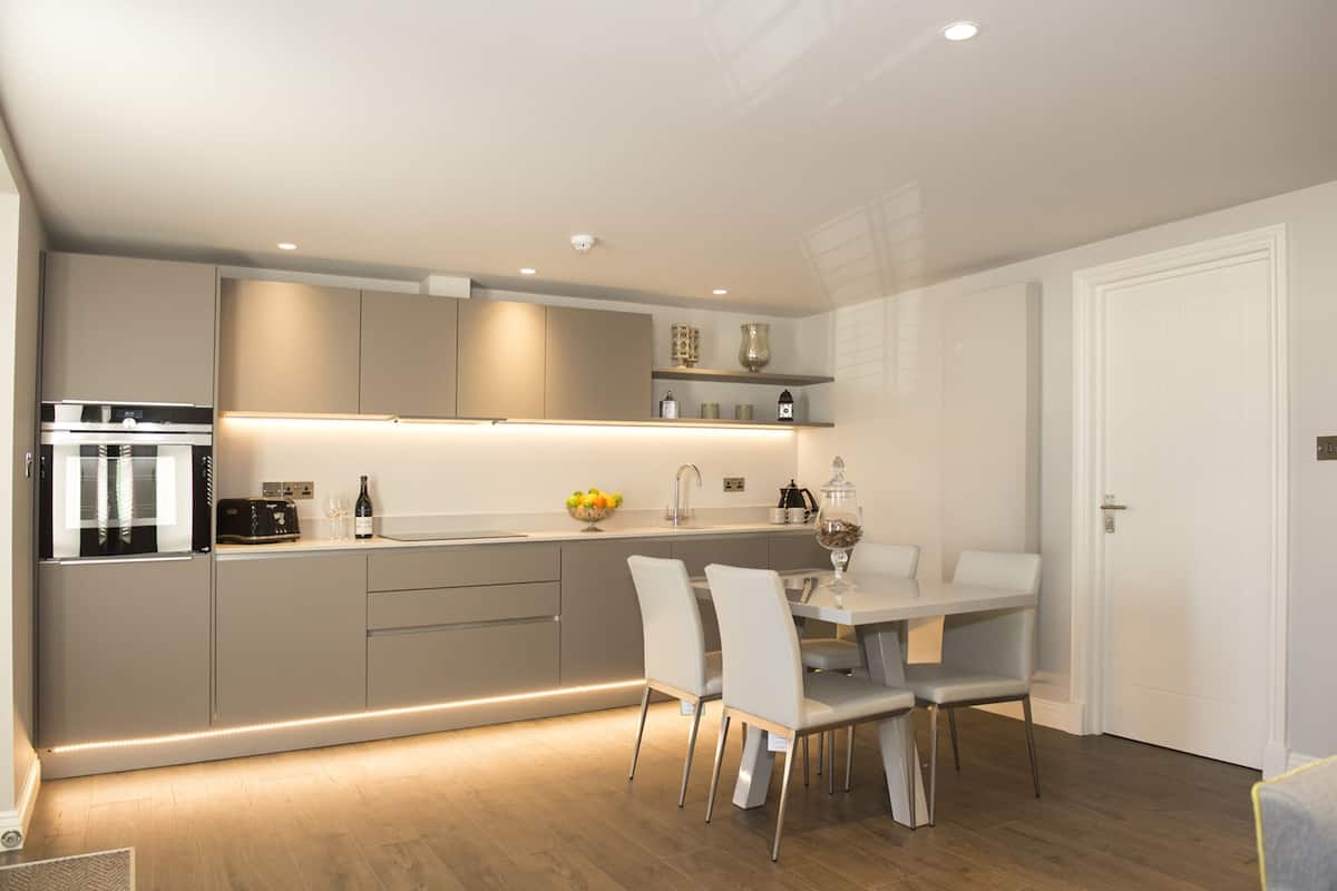 Une cuisine moderne dotée d’un four encastré, un coin repas avec une table et des chaises blanches, et une porte blanche.