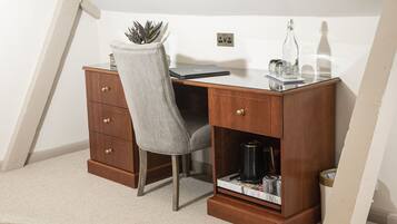 A corner desk with a chair, a small cabinet, and a shelf with books and a lamp.
