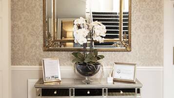 A reception area with a large mirror, a console table with a vase of flowers, and a chandelier.