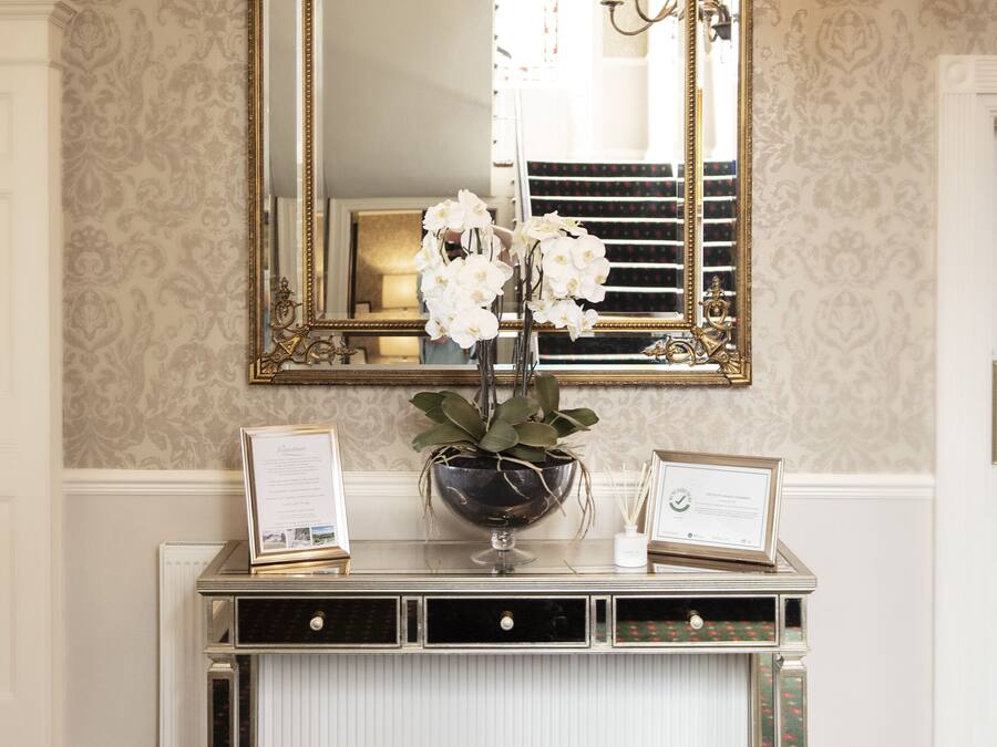 A reception area with a large mirror, a console table with a vase of flowers, and a chandelier.
