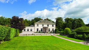 A large, stately building with a symmetrical facade, a central entrance, and a well-manicured lawn in front.