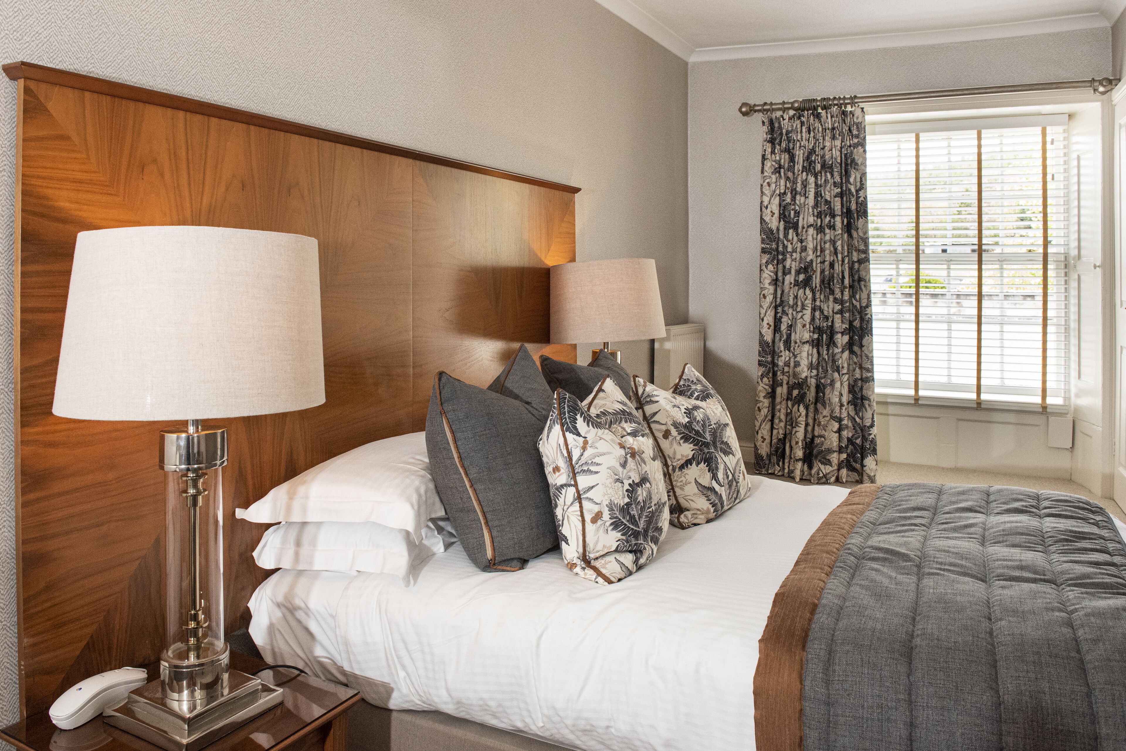 A hotel room with a wooden headboard, two bedside lamps, a telephone, and a window with curtains.