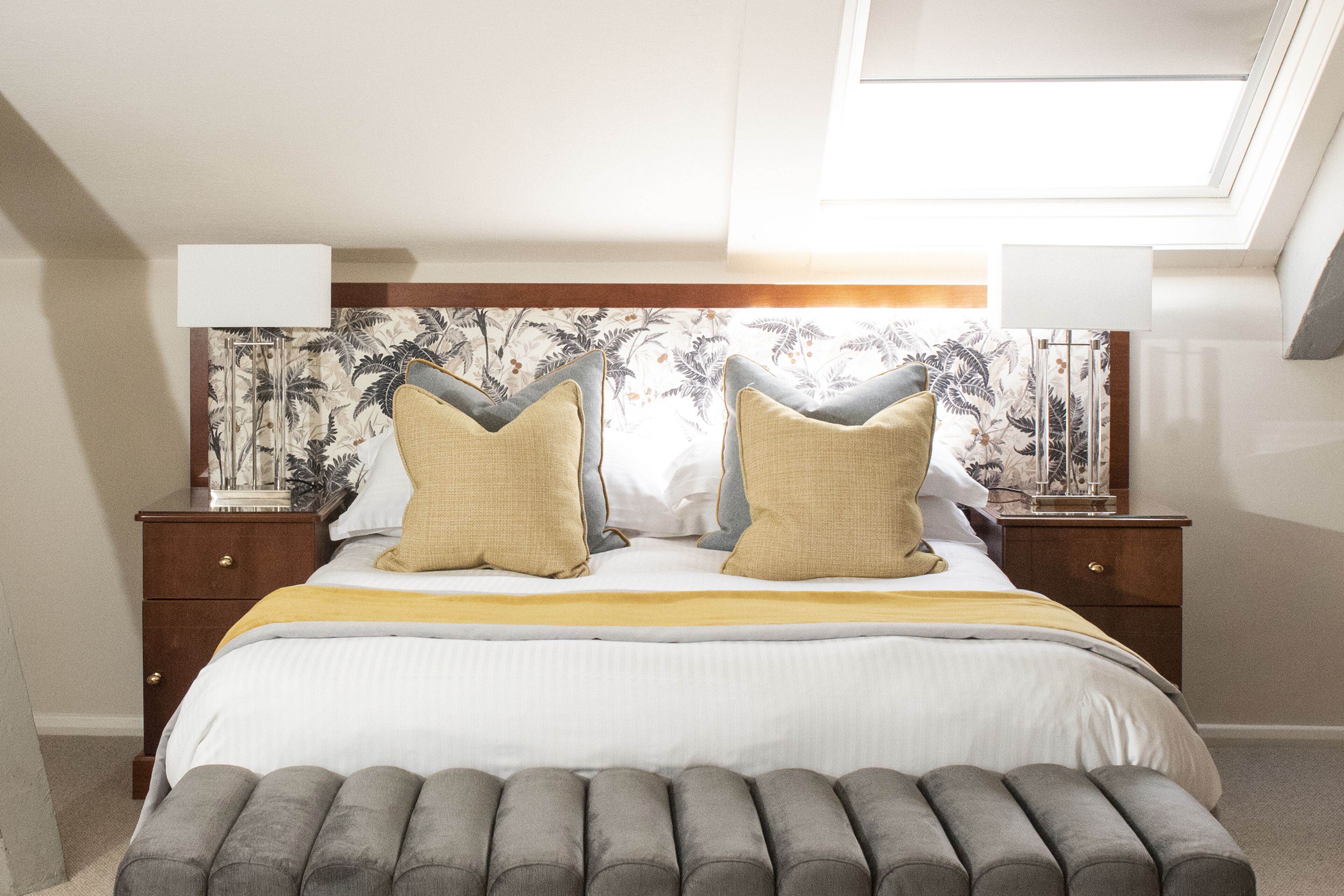 A bedroom with a bed, two nightstands, a lamp, and a skylight.