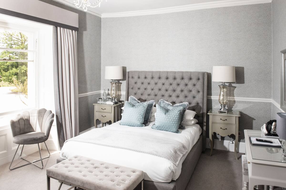 Une chambre avec un grand lit, deux tables de chevet avec des lampes, une chaise et une fenêtre avec des rideaux.