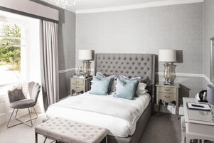 Un dormitorio con una cama grande, dos mesitas de noche con lámparas, una silla y una ventana con cortinas.