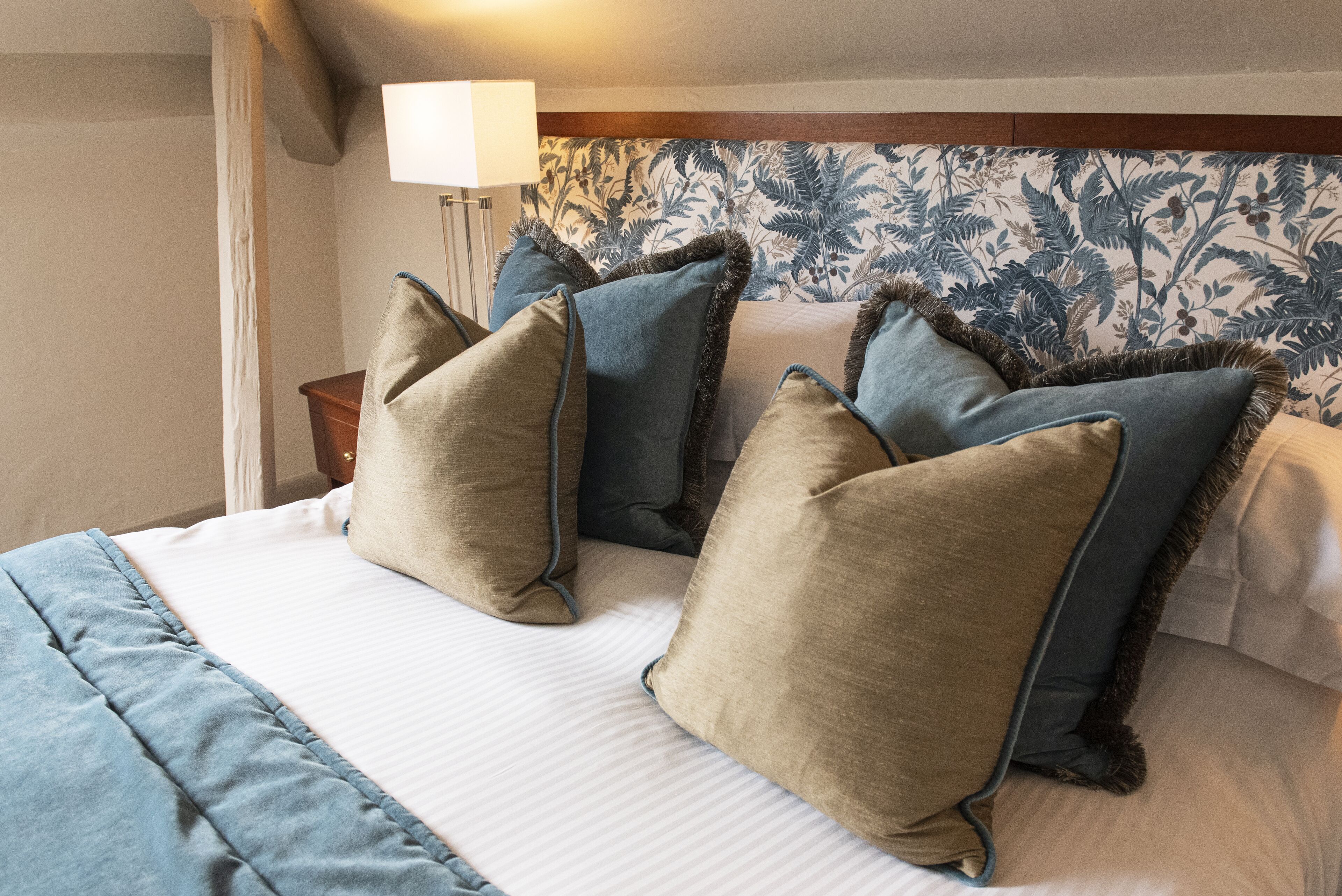 Un lit bien fait, recouvert d’une couvre-lit à rayures blanches et bleues, avec deux oreillers beige et un oreiller bleu bordé d’un galon foncé.
