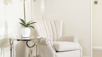 Un rincón de una habitación con un sillón blanco, una mesita redonda con una lámpara y una planta en maceta.