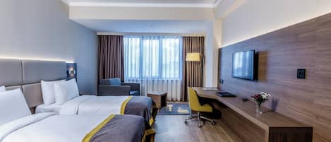 Habitación de hotel con dos camas, un escritorio, una silla, un televisor y una ventana con cortinas.