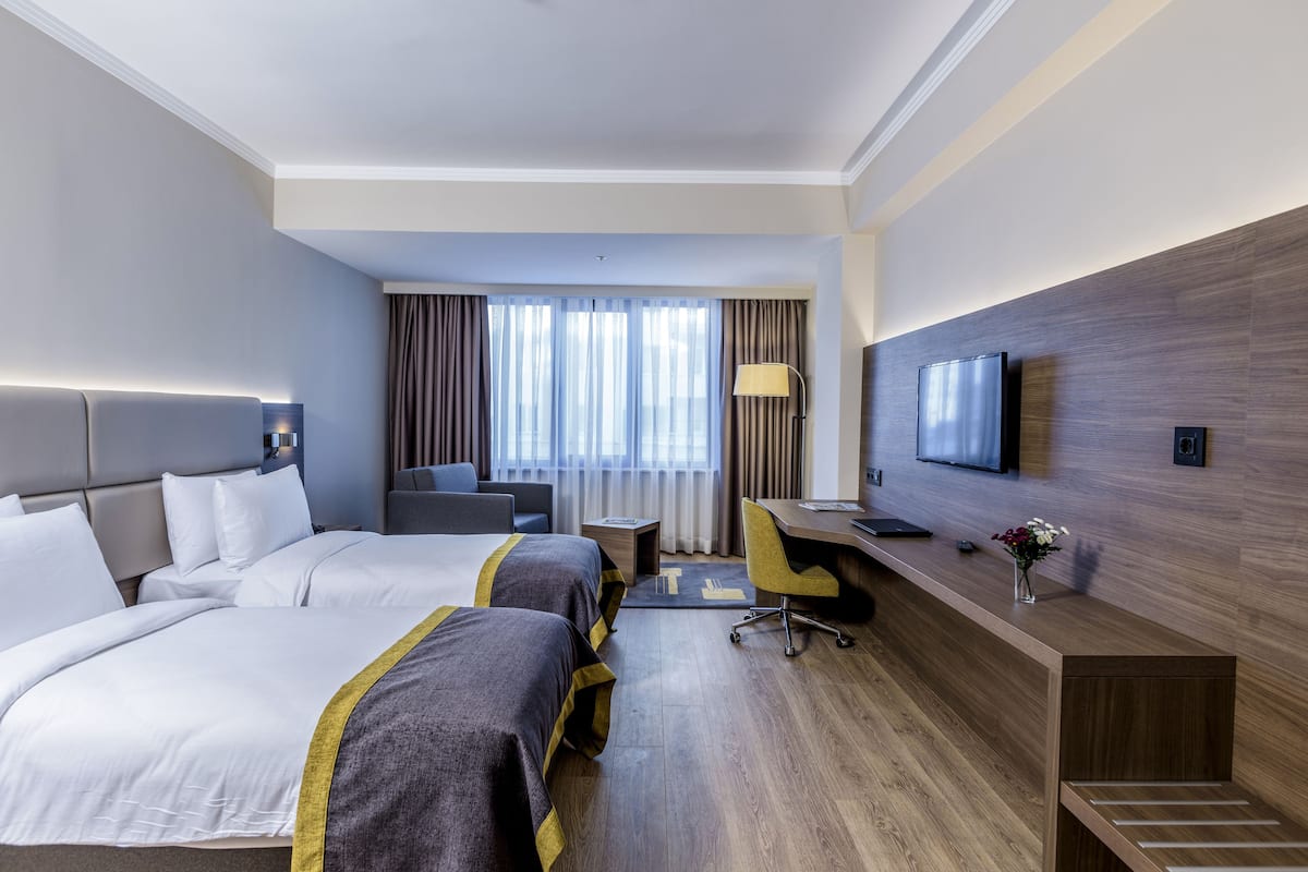 A hotel room with two beds, a desk, a chair, a TV, and a window with curtains.