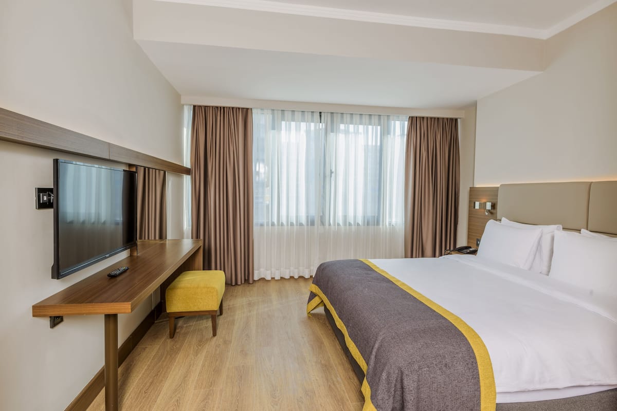 A hotel room with a bed, a TV, a desk, and a window with curtains.