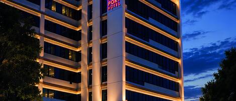A multi-story hotel with a prominent sign, a paved entrance, and a parked car.