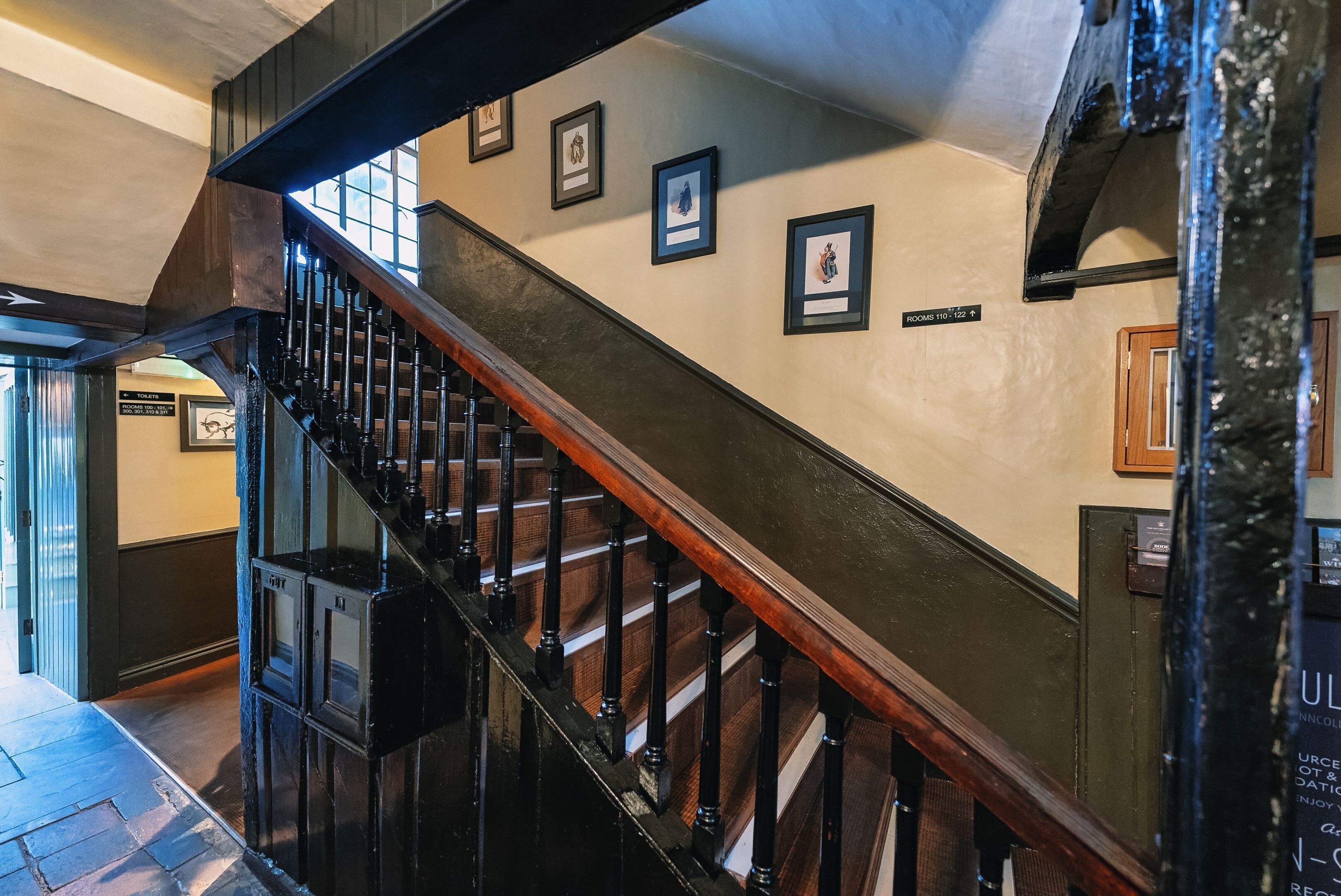 A staircase with wooden railings and a black handrail, leading to a room labeled "ROOMS 110-122".