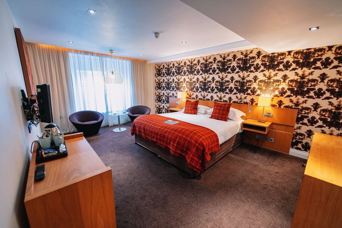 A hotel room with a large bed, a desk with a computer, a chair, and a small table.
