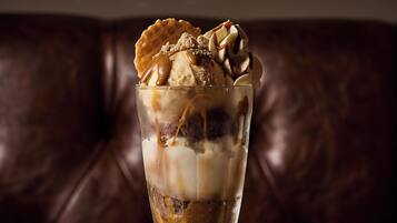 A dessert in a tall glass on a wooden table with a brown leather couch in the background.