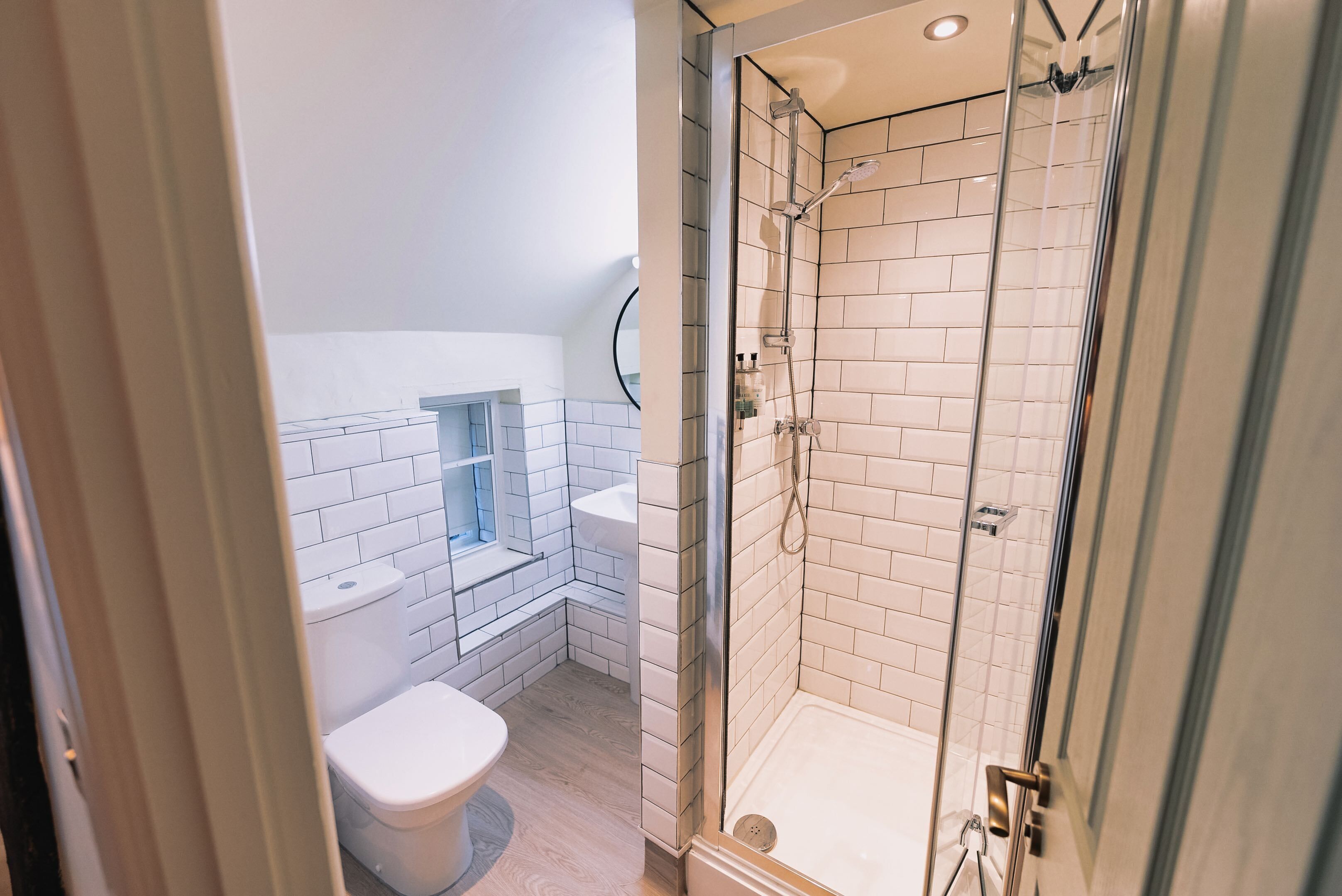 A modern bathroom with a glass-enclosed shower, white tiled walls, a toilet, and a sink.