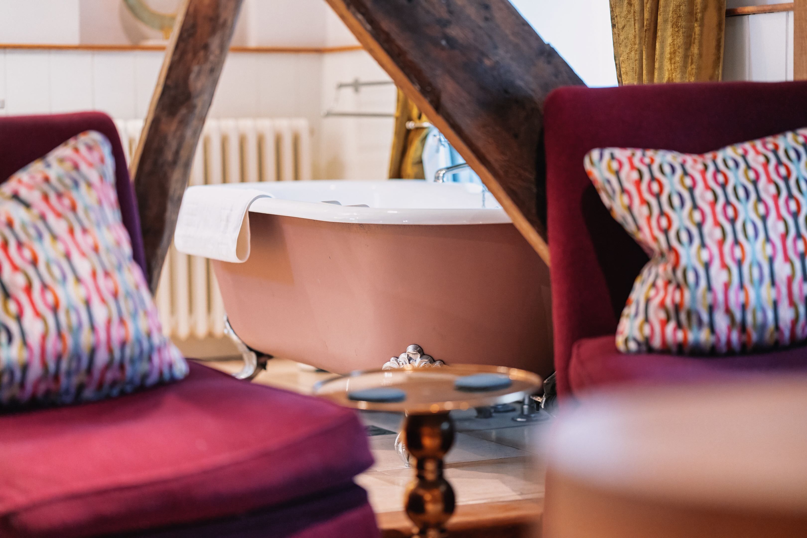 Een badkamer met een bad, een houten stoel en een gekleurd kussen.