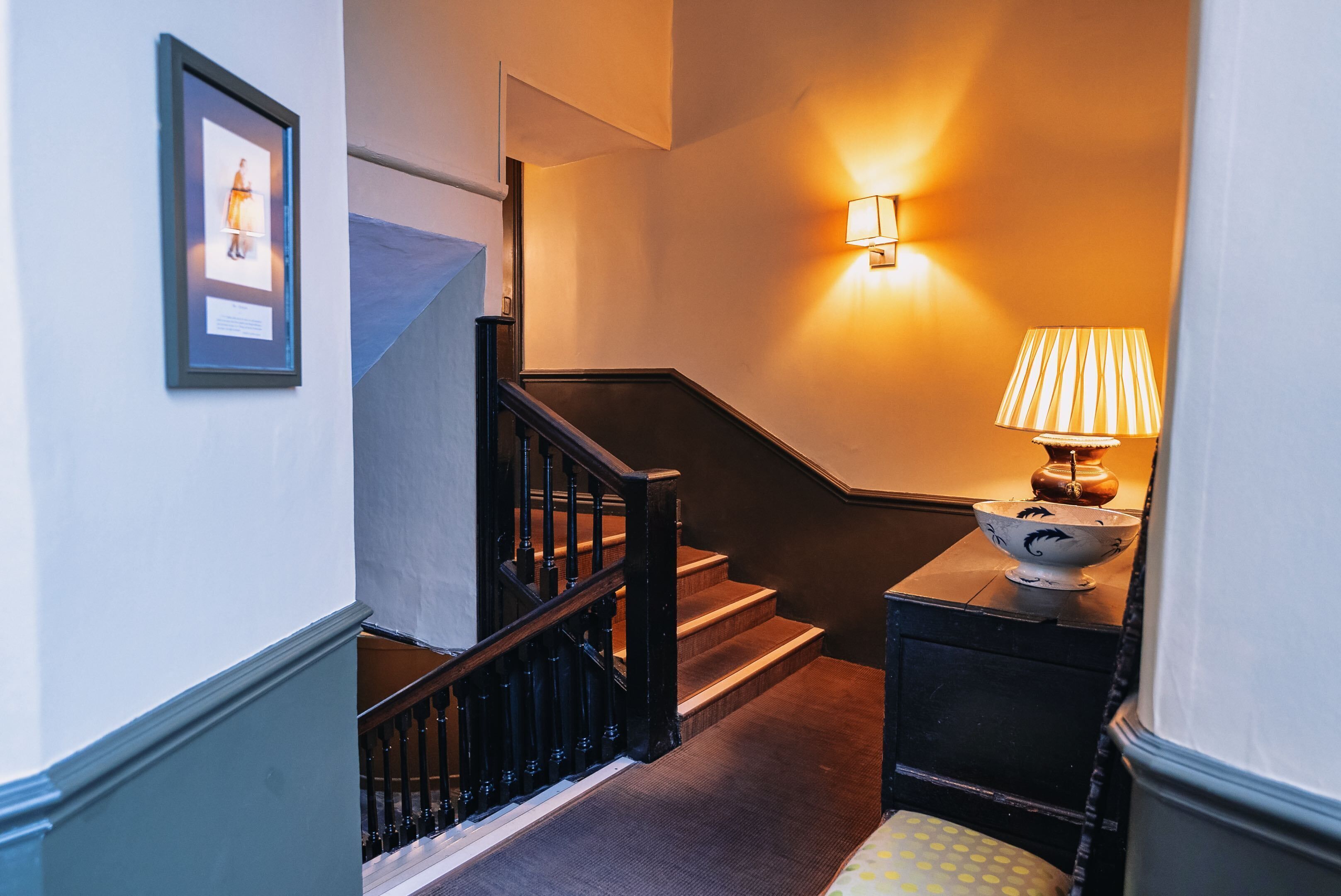 A staircase with a black railing, a wall-mounted lamp, and a framed picture.
