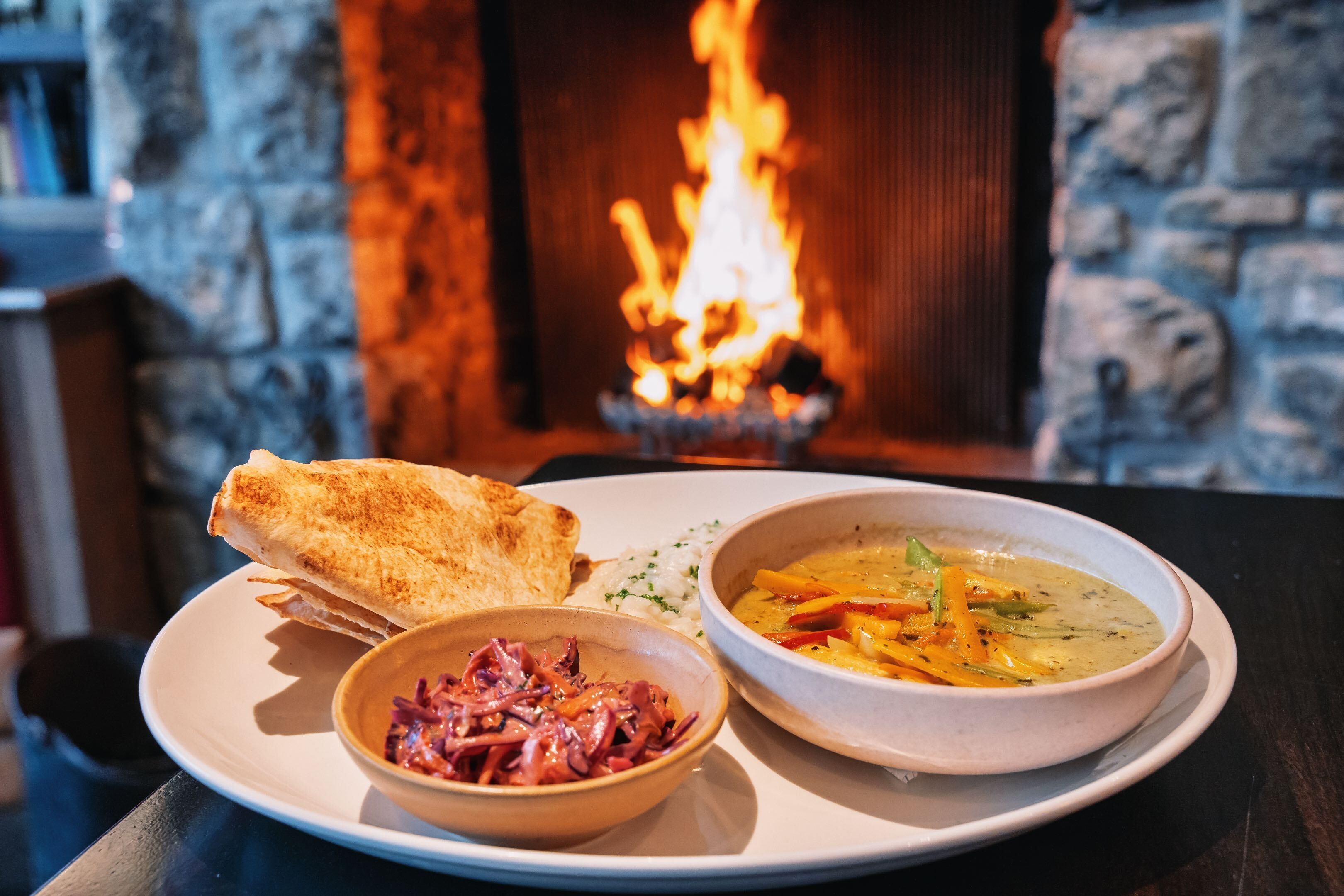 A plate with a grilled sandwich, a bowl of soup, and a side of pickled vegetables.