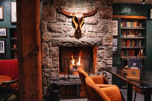 A stone fireplace with a large bull's head above it, a bookshelf to the right, and a red booth in the foreground. - The Bull and Townhouse, Beaumaris- The Inn Collection Group (Beaumaris)