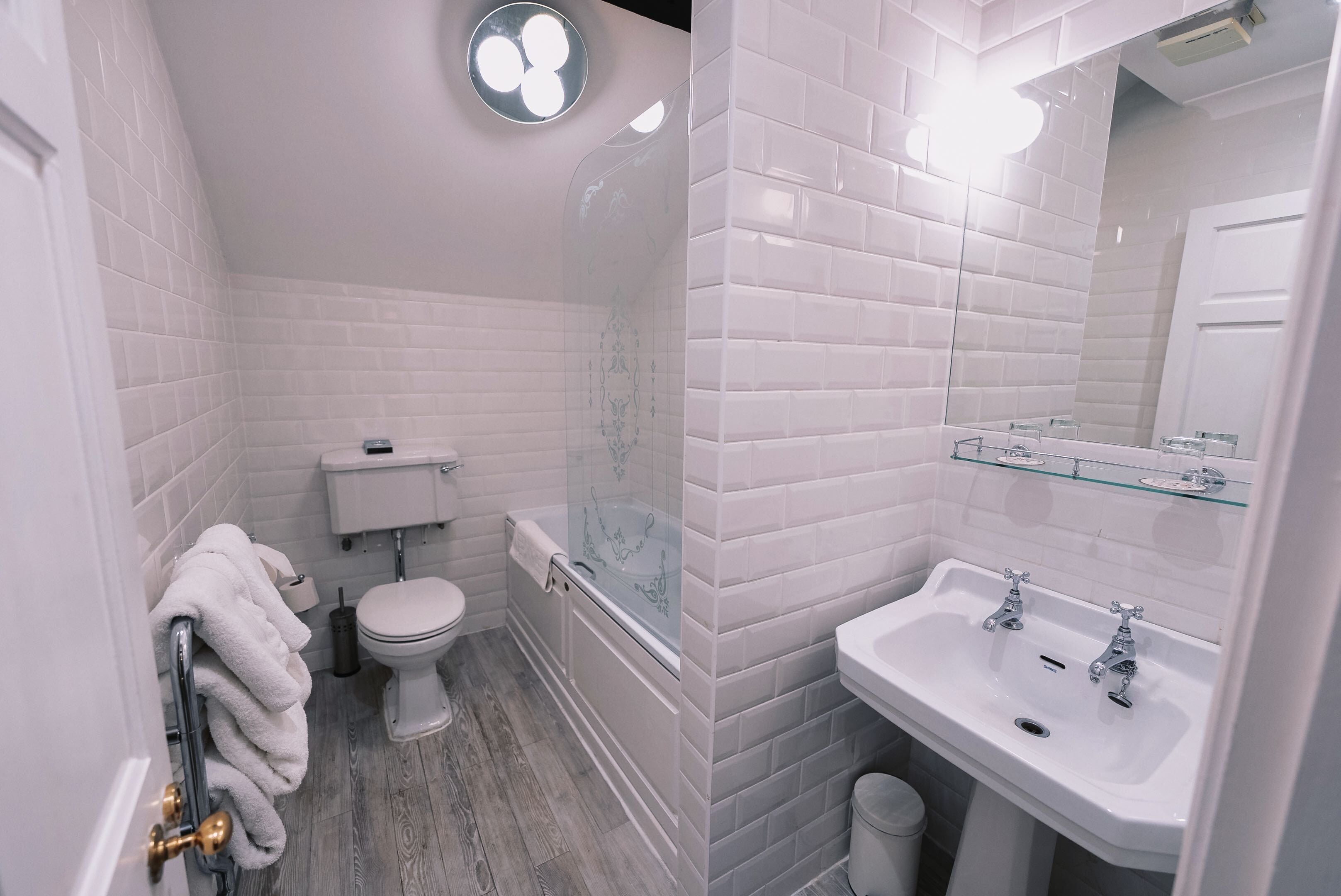 A bathroom with white tiled walls, a toilet, a bathtub, and a sink with a mirror.